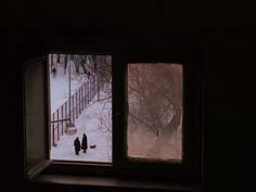 two people standing in front of a window with snow on the ground