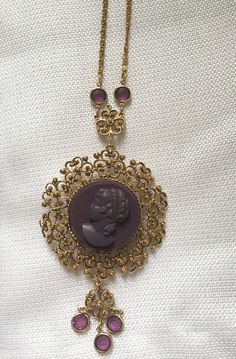 "Gorgeous 1950's statement watch pendant/necklace. Large gold plated medallion features a purple high relief carved profile cameo. Dangling down and attached to the chain are 7 round faux amethysts set in bezels. Lovely specialty chain has a large spring ring closure. The back has a Medana 17 Jewel mechanical wind watch, working well and winds easy. Necklace is 32\" long The pendant is 2 1/2\" in diameter My husband Alan & I had a brick & mortar store in Center City Philadelphia, on Jewe Vintage Antique Gold Cabochon Jewelry, Antique Yellow Gold Medallion Necklace, Vintage Yellow Gold Cabochon Necklace, Victorian Jewelry With Large Medallion Pendant, Vintage Costume Jewelry Medallion Necklace, Vintage Medallion Costume Jewelry Necklace, Ornate Yellow Gold Jewelry Vintage Collection, Costume Jewelry Medallion With Vintage Charm, Vintage Charm Medallion Costume Jewelry