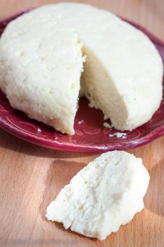 a red plate topped with cheese next to a piece of bread on top of a wooden table