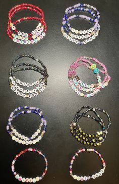 six beaded bracelets are arranged on a black surface and one has a flower in the middle