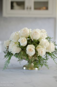 white roses and greenery in a silver vase on a marble countertop with cabinets