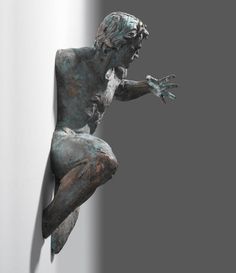 a bronze statue of a man leaning against a wall with his hands in the air