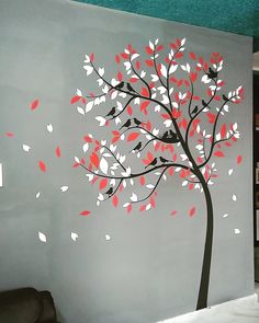 a tree with red and white leaves blowing in the wind on a gray wall next to a black chair