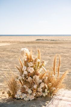 an arrangement of flowers and grasses on the beach