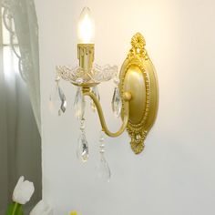 a gold wall light with crystal drops hanging from it's side, next to a white flower