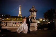 a bride and groom walking together in front of the eiffel tower at night