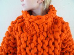 a woman is wearing an orange knitted coat with braids on the shoulders and neck