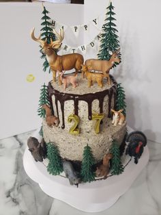 a birthday cake decorated with deer and trees on top of a marble slab topped with white frosting