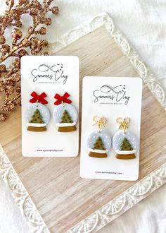 two snow globe earrings with bows on them sitting next to a christmas ornament