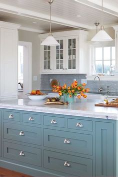 a kitchen with blue cabinets and an island in the middle is decorated with orange flowers