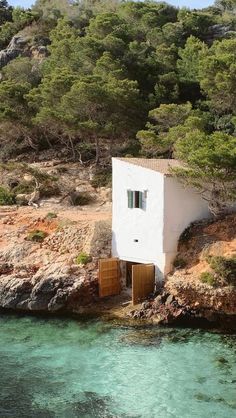 a small white house sitting on top of a cliff next to the ocean and trees