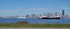 two large ships in the water near a city with tall buildings and green grass on both sides