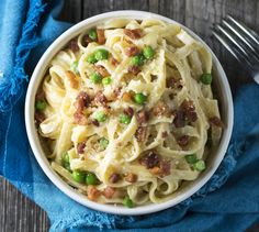 a white bowl filled with pasta and peas on top of a blue napkin next to a fork