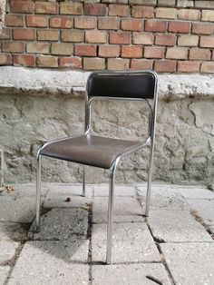 a metal chair sitting on the sidewalk next to a brick wall