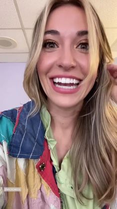 a woman with blonde hair is smiling and wearing a colorful shirt in front of a mirror