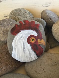 a painted rock with a rooster's head on it and some rocks around it