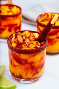 two glasses filled with food and garnish on top of a white table next to lime wedges