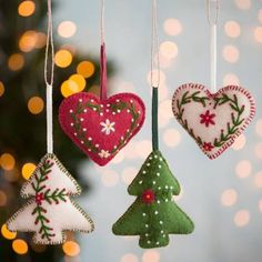 three christmas ornaments hanging from strings in front of a christmas tree with lights behind them