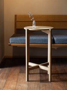 a wooden table with a glass vase on it sitting next to a blue bench in a room