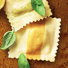 two ravioli shells with basil leaves on top and lemon wedges next to them