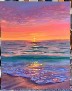 an easel with a painting on it and the sun setting over the ocean in the background