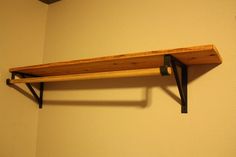 a wooden shelf mounted to the side of a wall with two black brackets on it