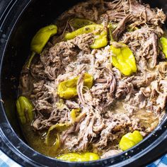 a slow cooker filled with meat, peppers and pickles on a blue checkered table cloth