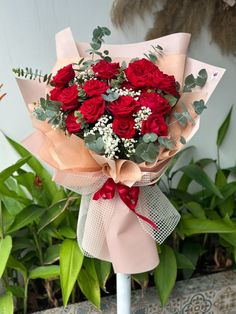 a bouquet of red roses with greenery on the table in front of some plants