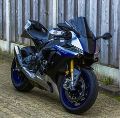 a blue and silver motorcycle parked next to a wooden fence