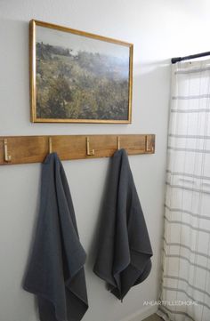 two towels are hanging on the hooks in front of a painting and a shower curtain