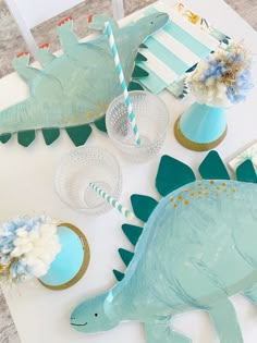 a table topped with paper plates and cups filled with cake toppers next to dinosaur decorations