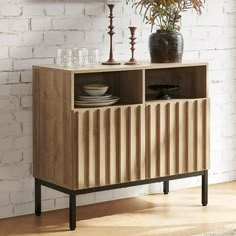 a wooden cabinet sitting in front of a brick wall with plates and glasses on it