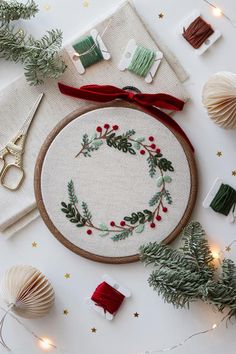 a cross stitch christmas wreath surrounded by other crafting supplies and holiday decorations on a white surface