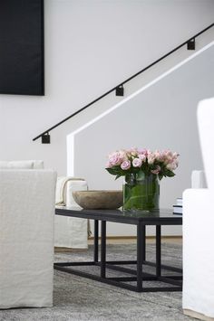 a glass vase with pink roses on a coffee table in a living room next to a white couch