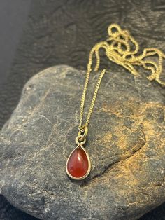 Carnelian is a gemstone known for its warm and fiery orange-red color. The drop pendant design adds an elegant and sophisticated touch to the necklace. Brass is a durable and affordable metal that complements the vibrant hue of the Carnelian. This necklace can be a statement piece, perfect for adding a pop of color and personality to any outfit. It can be worn for both casual and formal occasions, and its warm tones make it particularly suitable for autumn and winter seasons. 18" necklace Red Teardrop Gemstone Drop Necklace, Red Carnelian Oval Pendant Necklaces, Red Carnelian Teardrop Necklaces, Orange Oval Carnelian Necklaces, Red Carnelian Oval Pendant Necklace, Red Carnelian Oval Necklace, Red Carnelian Teardrop Necklace, Red Teardrop Gemstone Necklace, Amber Drop Gemstone Necklace