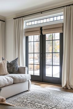 the living room is decorated in neutral colors and features an elegant rug, two large windows with drapes, and a white couch