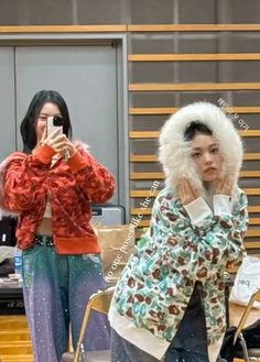 two women taking pictures with their cell phones in front of the camera while wearing winter clothing