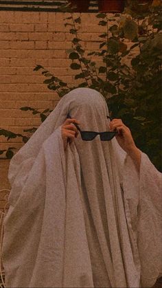 a person in a white cloak covering their face with a pair of black glasses on the ground