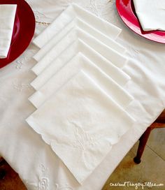 the table is set with white linens and red plates, napkins and utensils