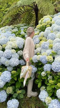 a woman is standing in the middle of blue and green flowers