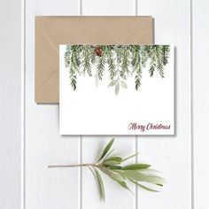 a christmas card with evergreen branches and pine cones hanging from it's side, on top of a brown envelope