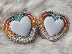 two white heart shaped brooches with multicolored beads on top of each other