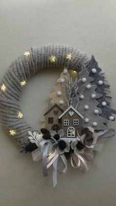 a christmas wreath with lights around it and a house on the front, surrounded by snowflakes