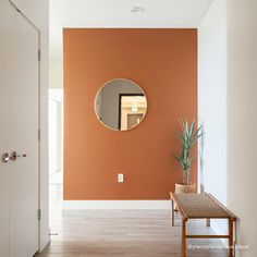 an orange wall with a mirror on it and a table in the hallway next to it