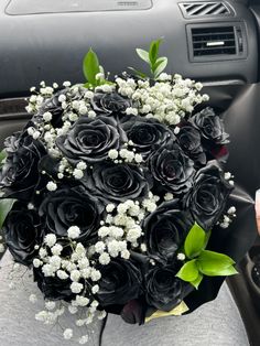 a bouquet of black roses and baby's breath in the back seat of a car