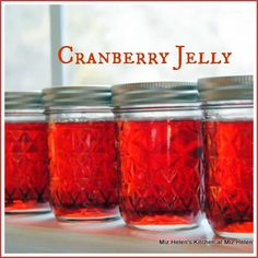 four jars with red liquid in them sitting on a window sill next to the words cranberry jelly