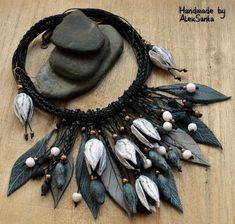 a black necklace with white beads and leaves on it is sitting on a wooden surface