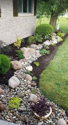 a garden with rocks and plants next to a house