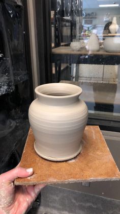 a person holding a clay pot on top of a piece of cardboard in front of a glass case