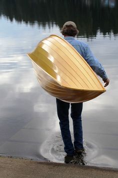 a man holding a wooden boat on top of a body of water next to a lake